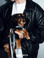Person holding a small dog wearing a leather jacket with 'KANAMUTA' branding.