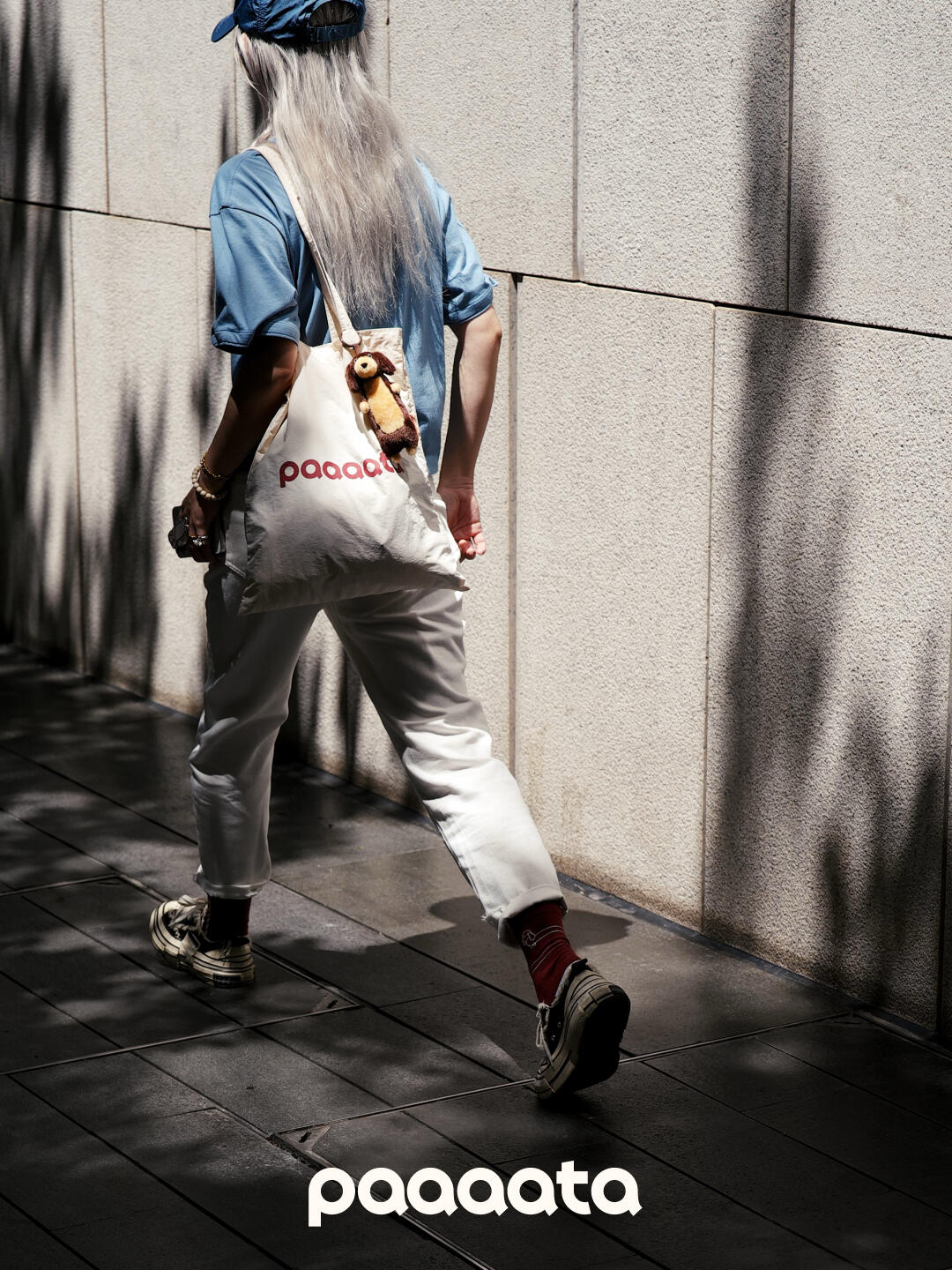 Person walking with a 'paaaata' bag against a textured wall