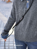 Person wearing a gray sweater with a black leash labeled 'Buddy Armor' on a blurred outdoor background.