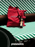 Red bag and plush toy on a green and white striped surface with 'paaaata' branding.