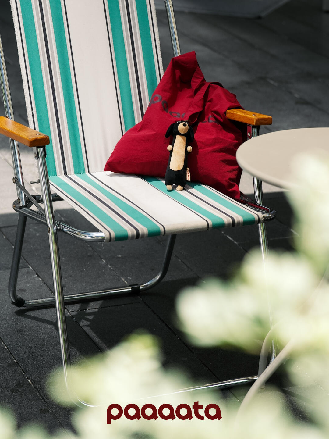 Striped beach chair with a red tote bag and small dachshund plush keychain on a dark surface, featuring the brand 'paaaata'.