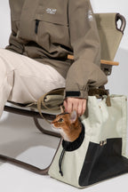 Person petting a cat through the side opening of a cat carrier tote, showing the adjustable opening with drawcord and the soft rim for comfort.