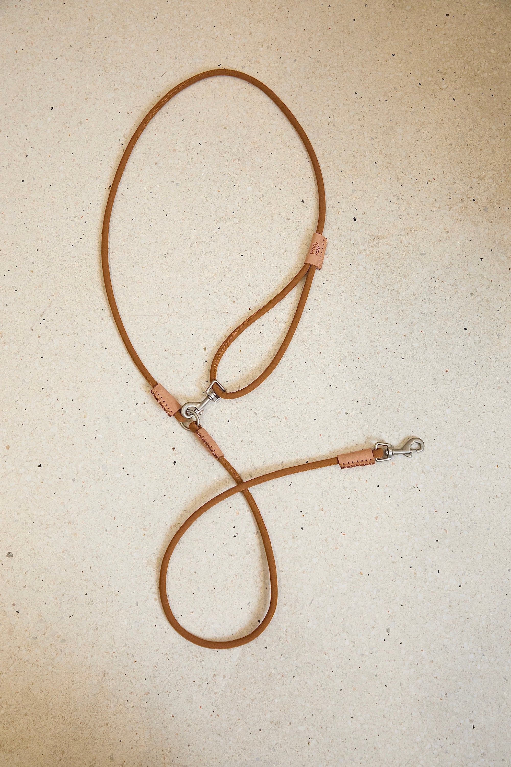 Crossbody dog leash displayed flat on a textured surface, showing adjustable length, soft matte rope texture, and minimal leather-trim details.