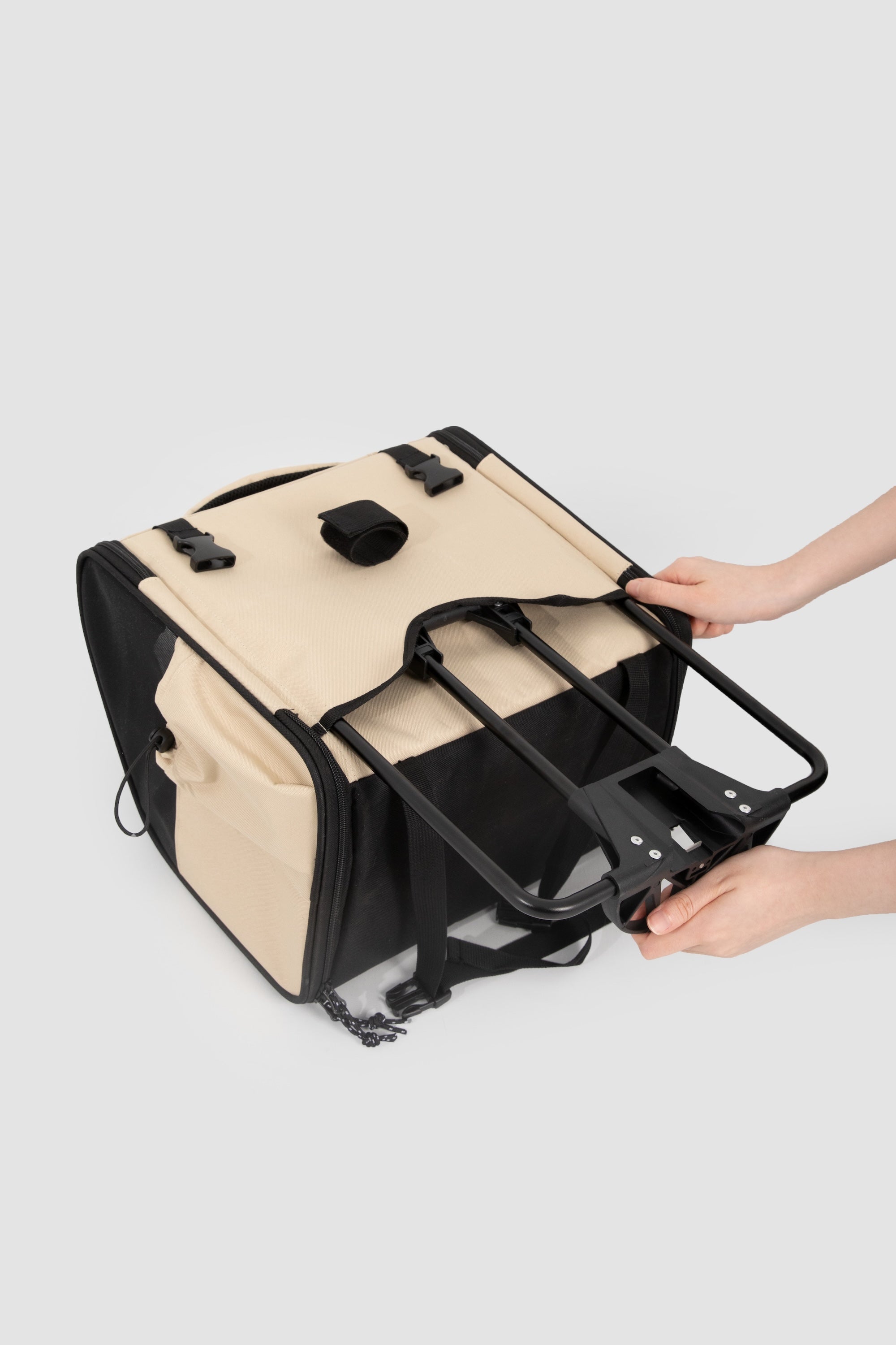 Hands attaching the metal support rack to the bottom of a dog bike carrier, showing how the pet bike bag is stabilized for riding.