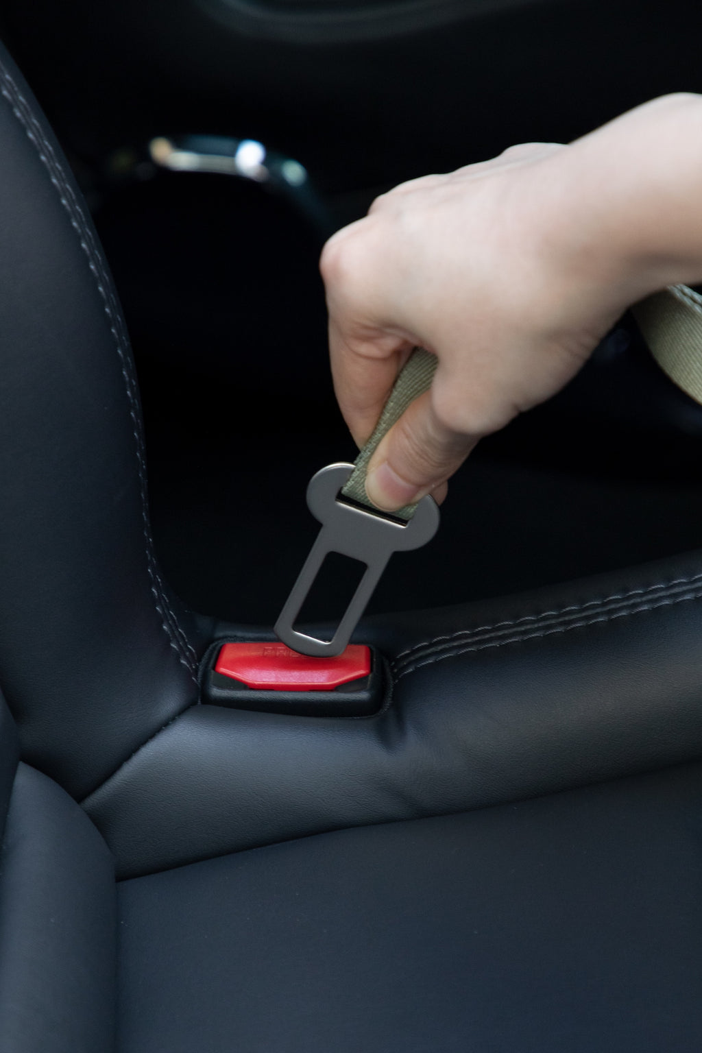 Hand inserting the dog car seatbelt tether into a standard car seat belt buckle, showing quick one-click attachment.