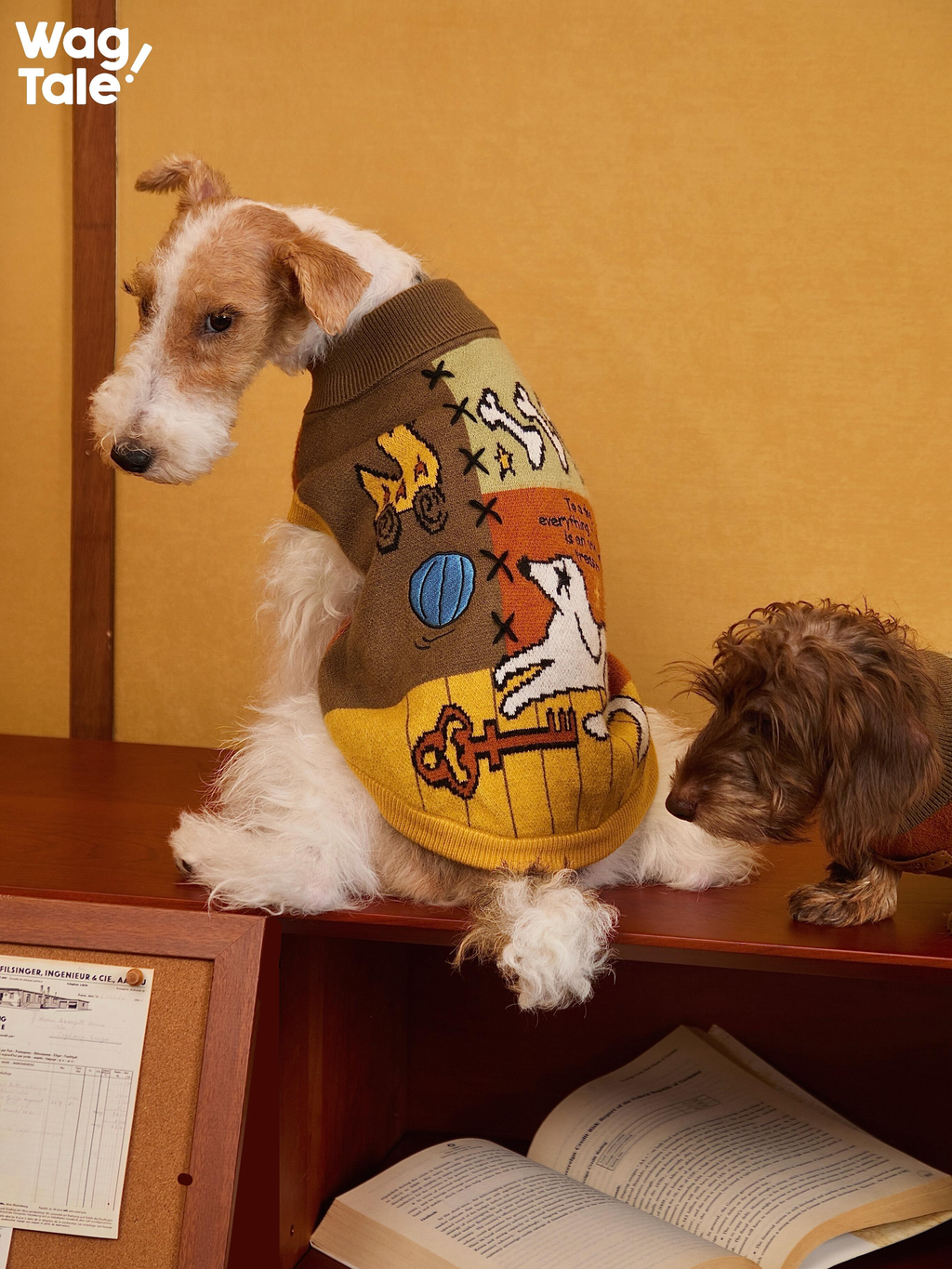 Terrier wearing an embroidered-style knitted dog sweater with multicolor yarn and graphic artwork; back view highlights the vintage pattern and warm knit construction.