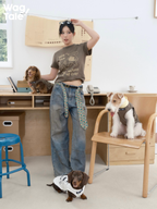 A person wearing a brown graphic cotton T-shirt poses indoors with multiple dogs, including a dachshund in a matching dog outfit, showing coordinated print styling.