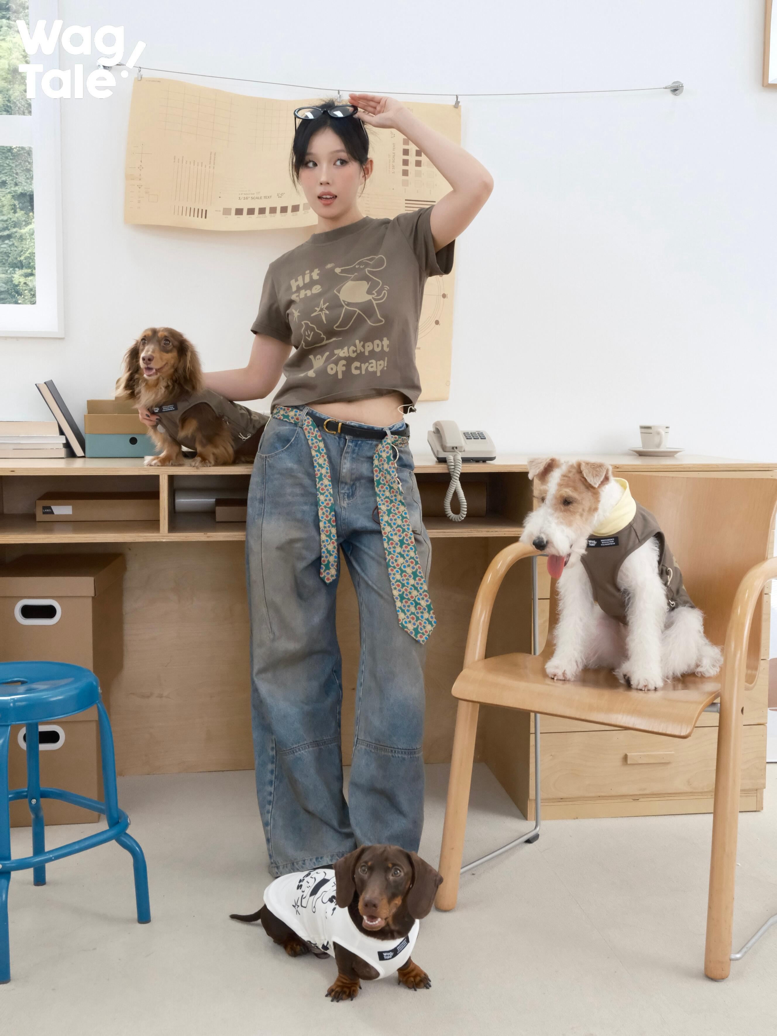 A person wearing a brown graphic cotton T-shirt poses indoors with multiple dogs, including a dachshund in a matching dog outfit, showing coordinated print styling.