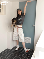 A person wearing a graphic cotton T-shirt stretches while holding a dog in a matching dog jumper, showing casual movement and coordinated outfit concept.