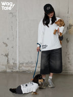 A person holding a dog in a graphic dog jumper while another dog wears the same style on the ground, showing everyday matching outfit concept.