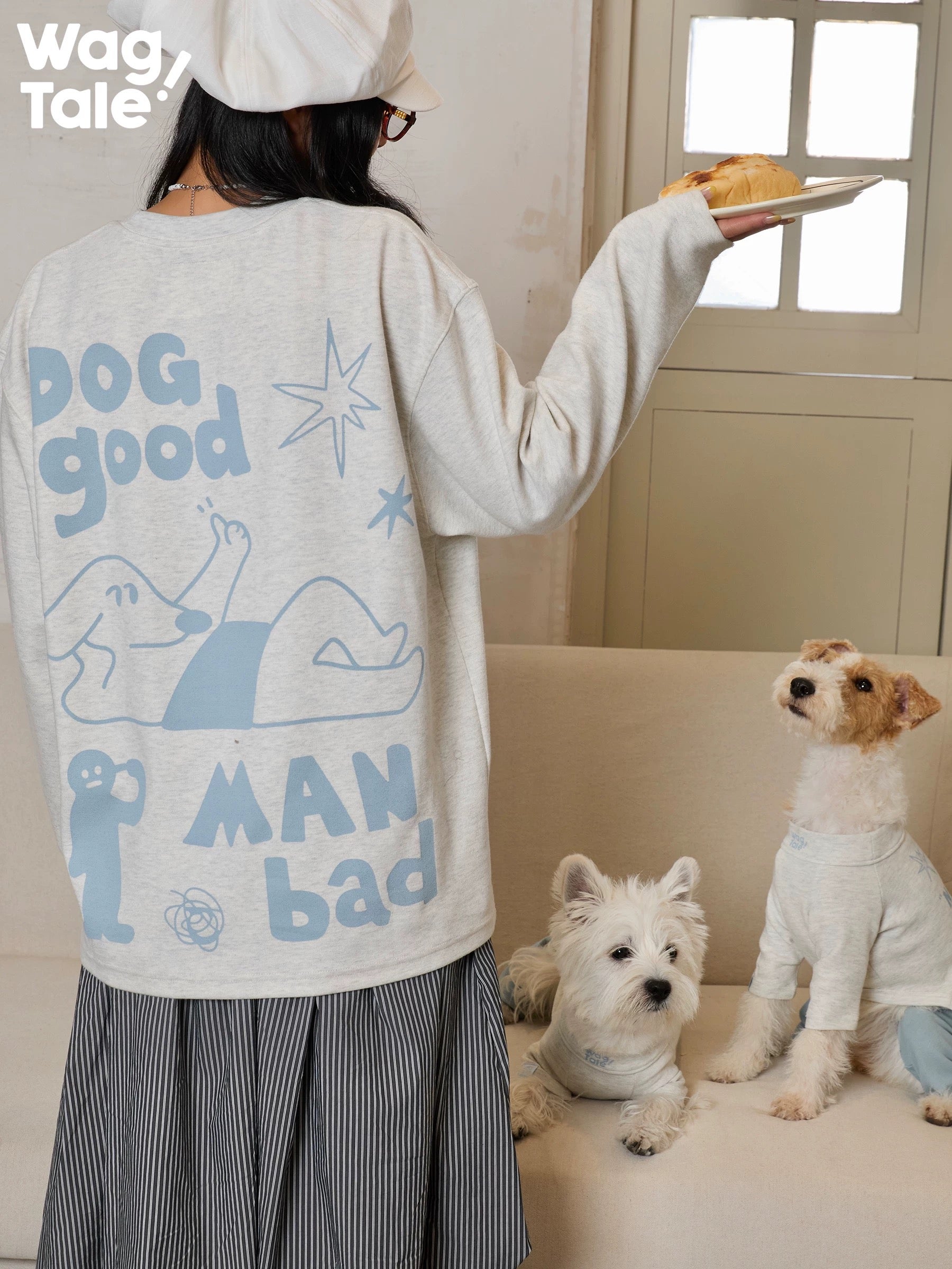 Indoor scene with a person wearing a graphic sweatshirt and dogs dressed in matching dog jumpers, highlighting playful illustration and relaxed styling.