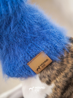 Close-up of Hound Co.'s leather brand label on a cobalt blue fuzzy snood, highlighting premium branding and craftsmanship for sighthound accessories.
