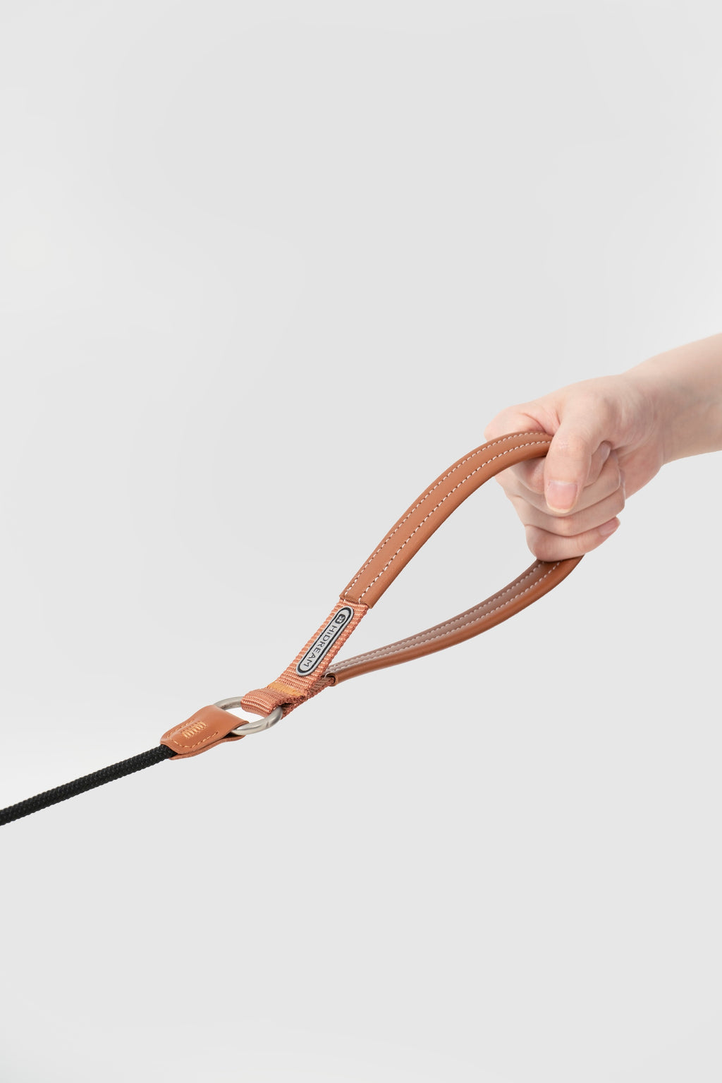 Hand holding the leather handle of a slip dog leash in brown, showing widened handle design for better grip and control.