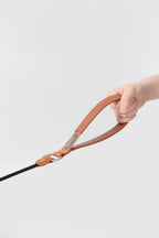 Hand holding the leather handle of a slip dog leash in brown, showing widened handle design for better grip and control.