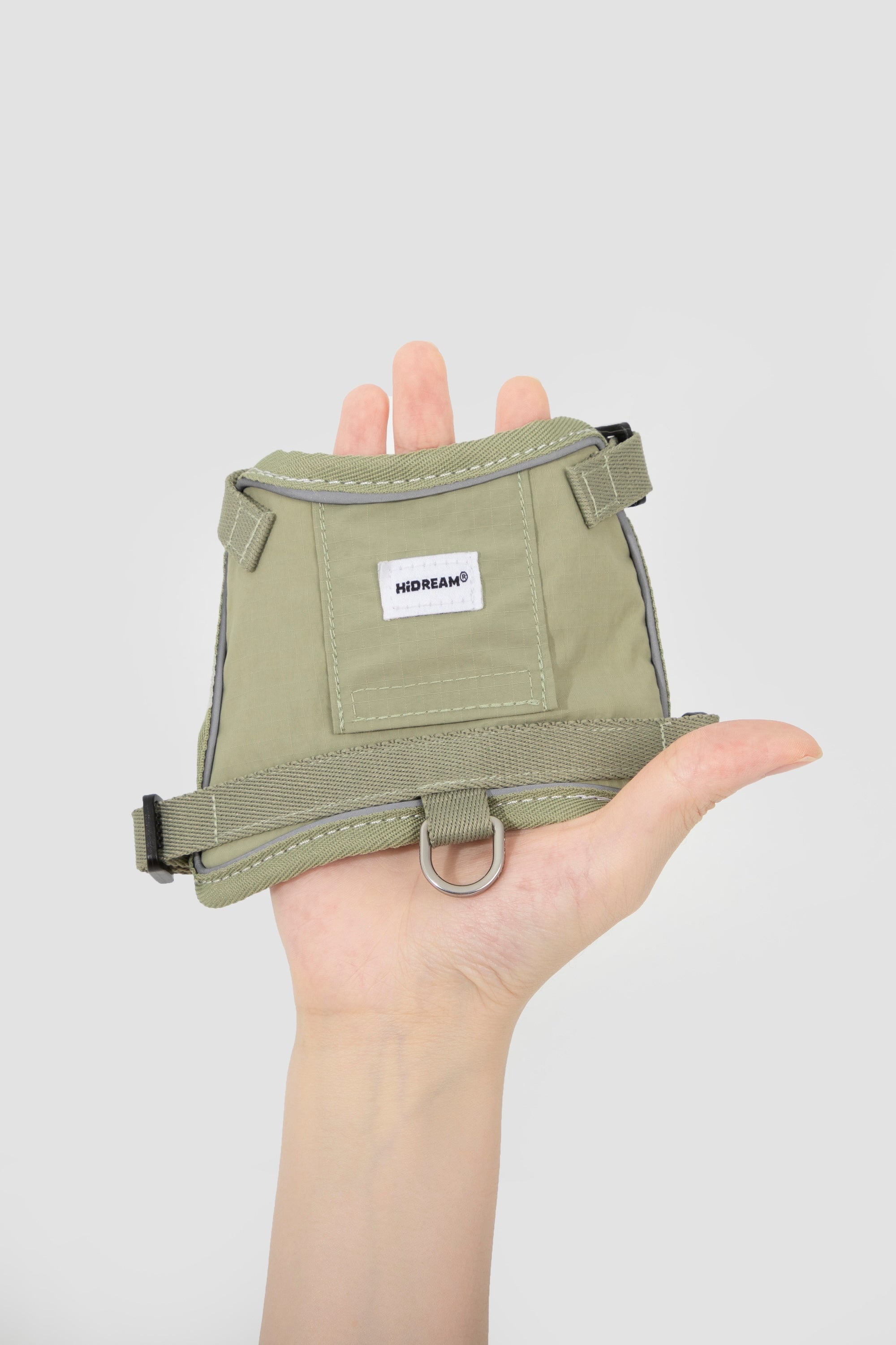 Hand holding an olive lightweight cat harness, showing compact size and front D-ring placement, designed as an escape-resistant cat harness for walking.