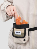 Close-up of a magnetic closure dog treat pouch worn on a waist belt, showing one-handed treat access with the wide opening and treat pieces inside.