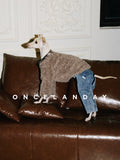 Italian Greyhound standing on a leather sofa wearing ONCELANDAY grey-brown lamb fleece dog jacket, showing textured fleece fabric in an indoor living room setting