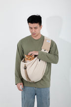 Man wearing a beige pet sling carrier on the front, gently holding an orange cat with its head visible above the opening, showing stable support and relaxed carry posture.