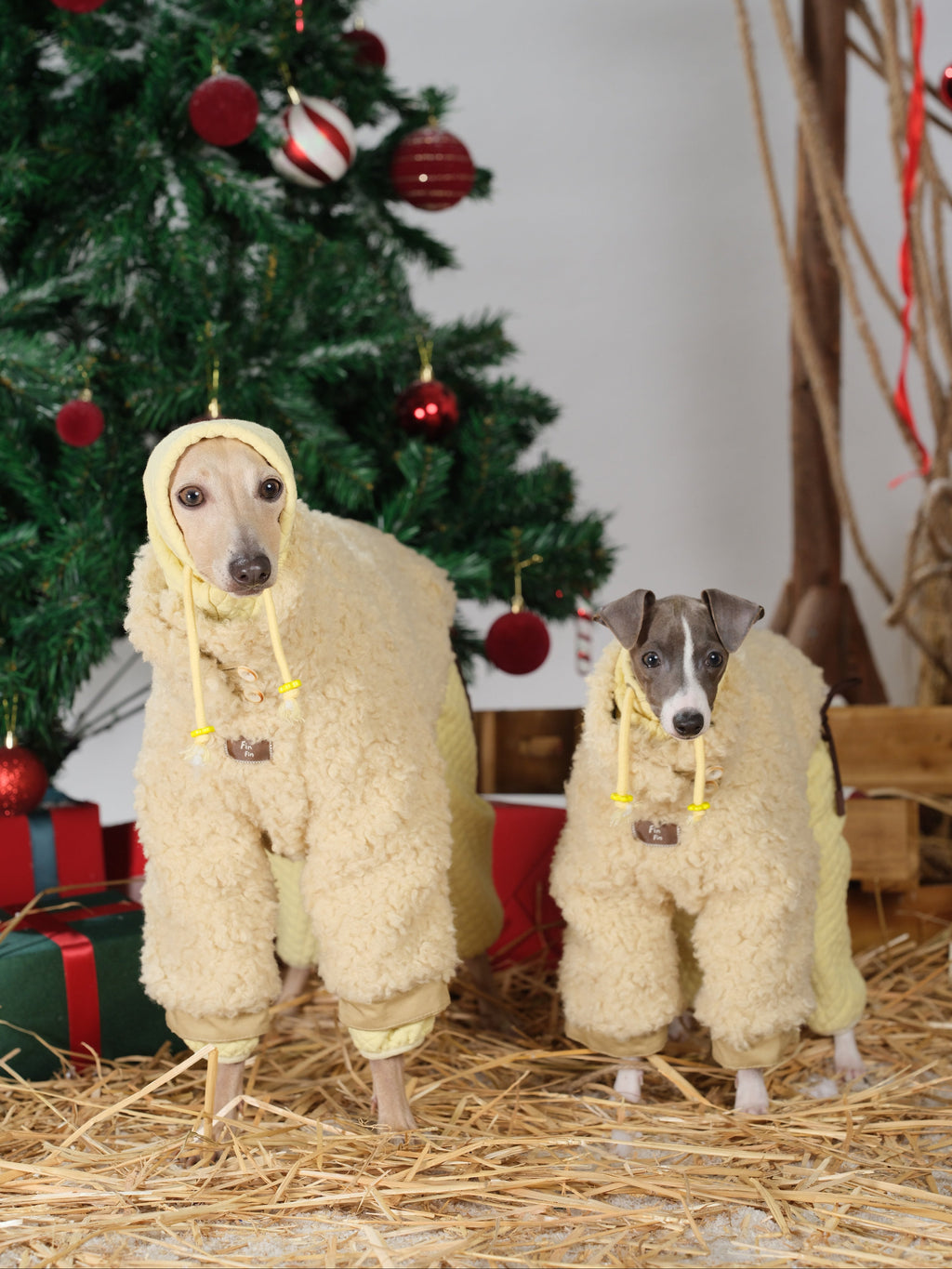 Two dogs wearing cream-colored fleece dog jackets standing in front of a Christmas tree, showing the cozy wool-blend fleece side in a festive indoor setting.