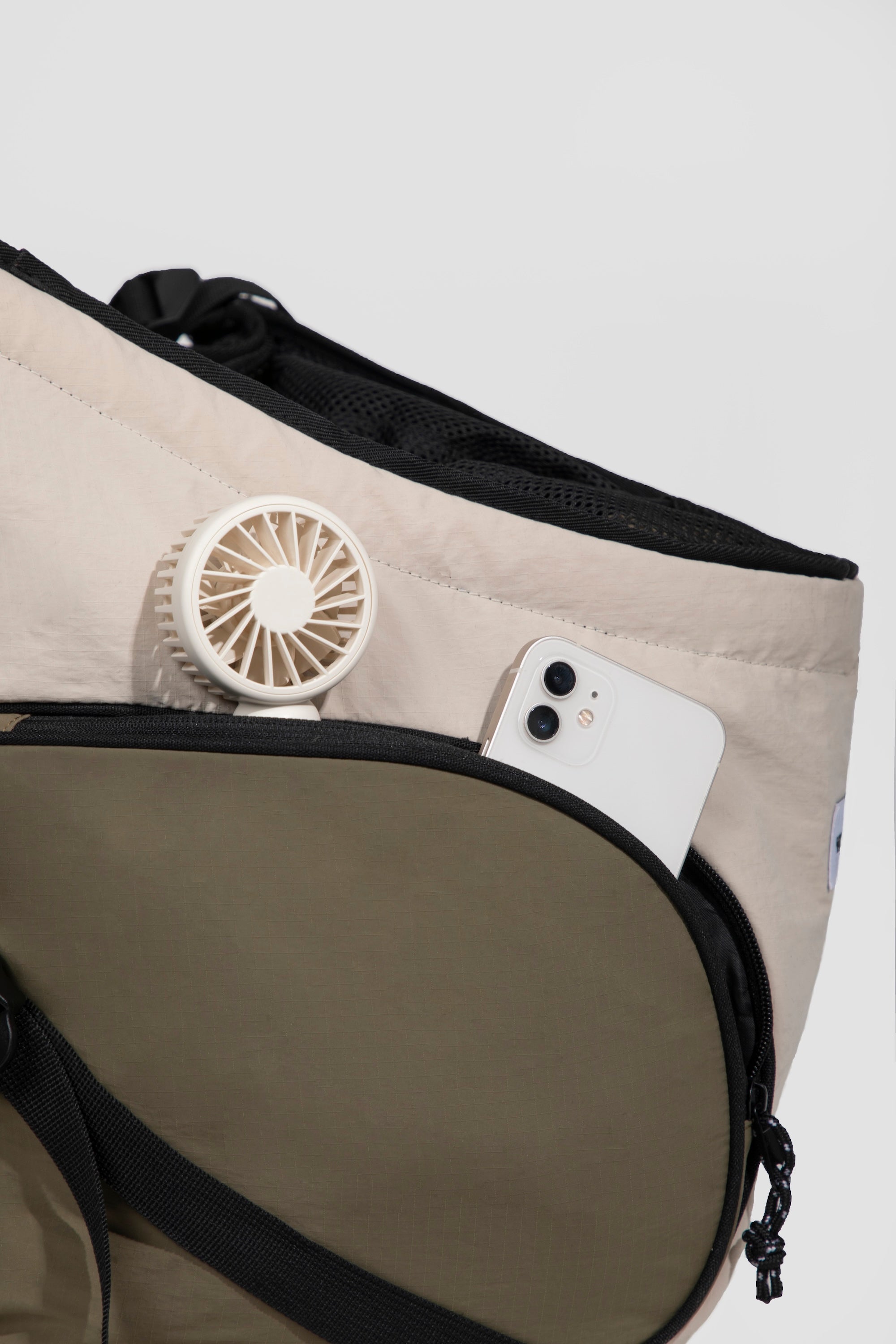 Side pocket of a front pet carrier holding a portable fan and smartphone, demonstrating practical storage for daily outings