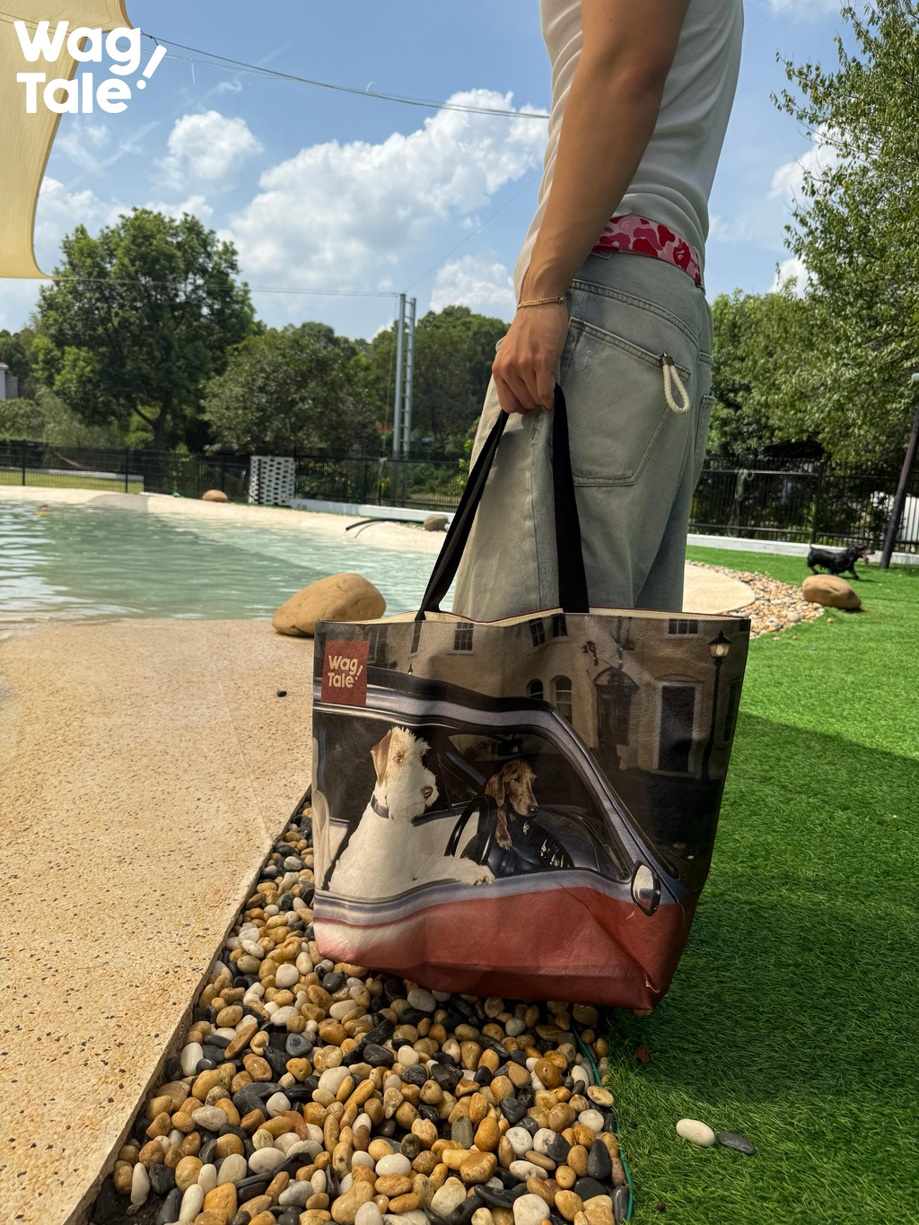 A person standing by a pool carrying a large travel tote bag on one shoulder, with the printed dog graphic visible against an outdoor setting.