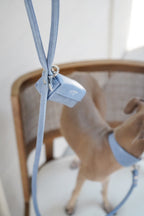 Close-up of a light blue vegan leather dog leash with a matching poop bag holder attached by a metal ring; microfiber texture and clean hardware detail shown.